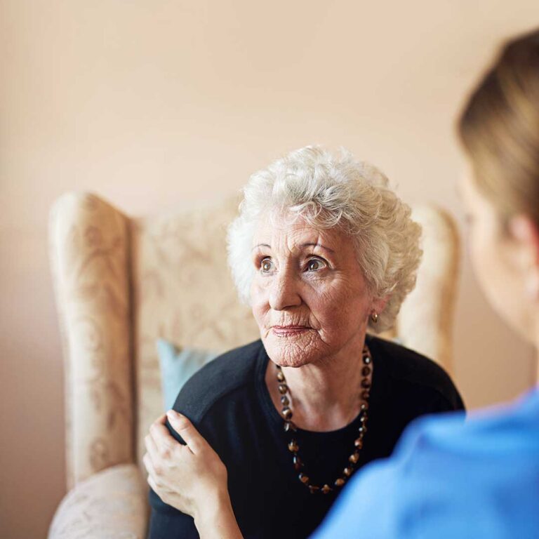 Two seniors sitting together in a comfortable living room, smiling and chatting with personal items around them.