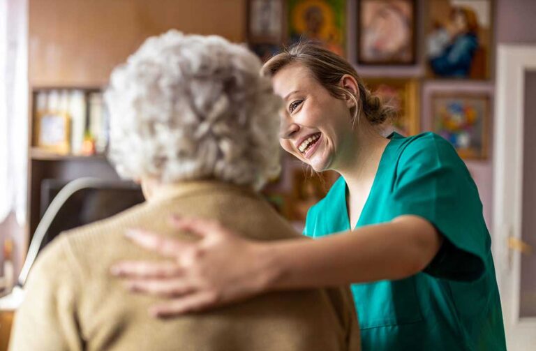 A senior resident sitting and talking with a caregiver at a table filled with paperwork and informational brochures.