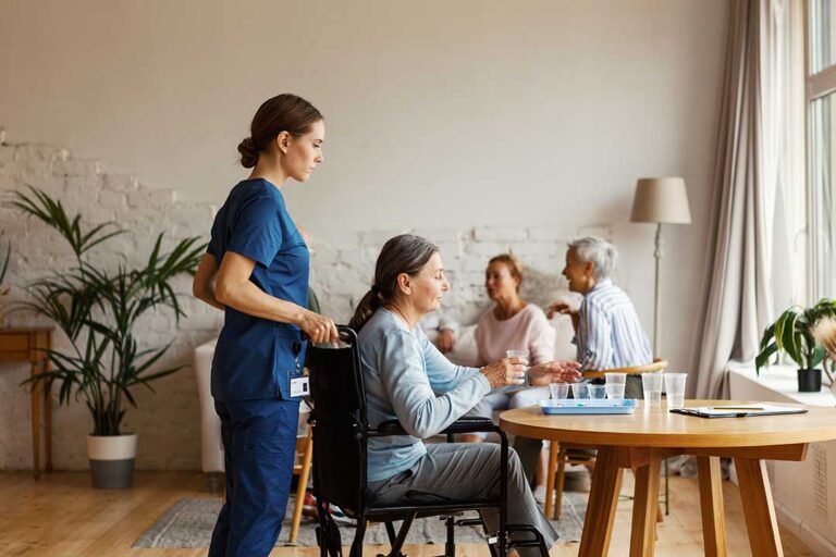 Older adult using a tablet beside a caregiver in a bright assisted living room.